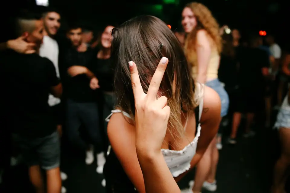 A guest making a peace sign, hair across her face, on a crowded dance floor